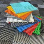 En livfull hög med färgglada sammankopplade plastgolvplattor, med nyanser av blått, orange, gult, vitt och grönt, lägger till en touch av kreativitet till garageinredningen på en texturerad svart och grå golvyta.