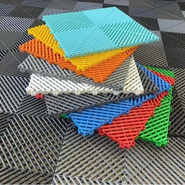En livfull hög med färgglada sammankopplade plastgolvplattor, med nyanser av blått, orange, gult, vitt och grönt, lägger till en touch av kreativitet till garageinredningen på en texturerad svart och grå golvyta.