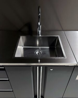 En modern garageinredning, har en diskbänk i rostfritt stål med en enkel kran, inställd i en elegant, mörk bänkskiva. Designen är minimalistisk, med rena linjer och en modern estetik.