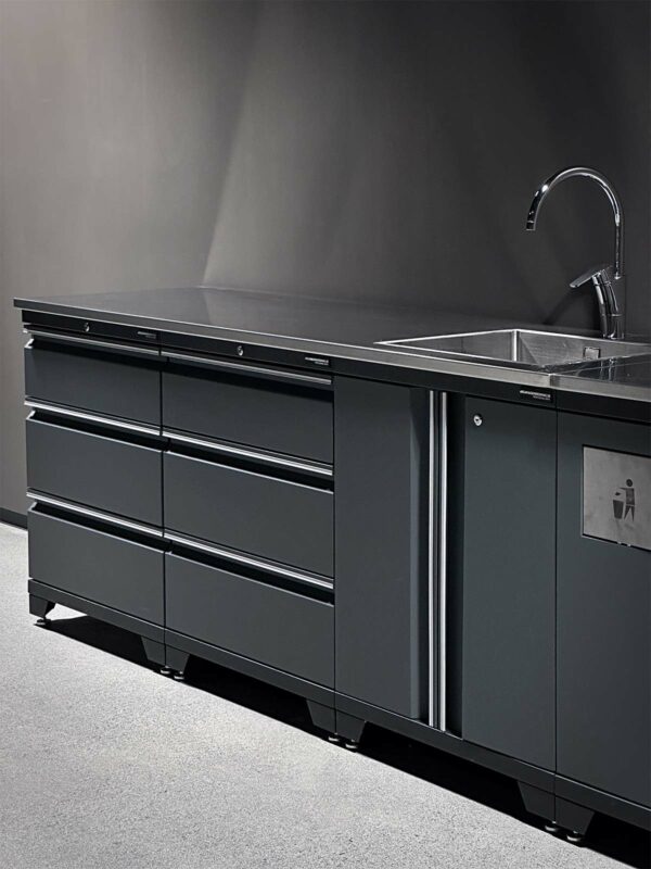 En elegant, mörkfärgad garageinredning med en polerad bänkskiva med handfat och kran. Det finns flera lådor och skåp för förvaring under bänkskivan. Arbetsytan har en minimalistisk och modern design.