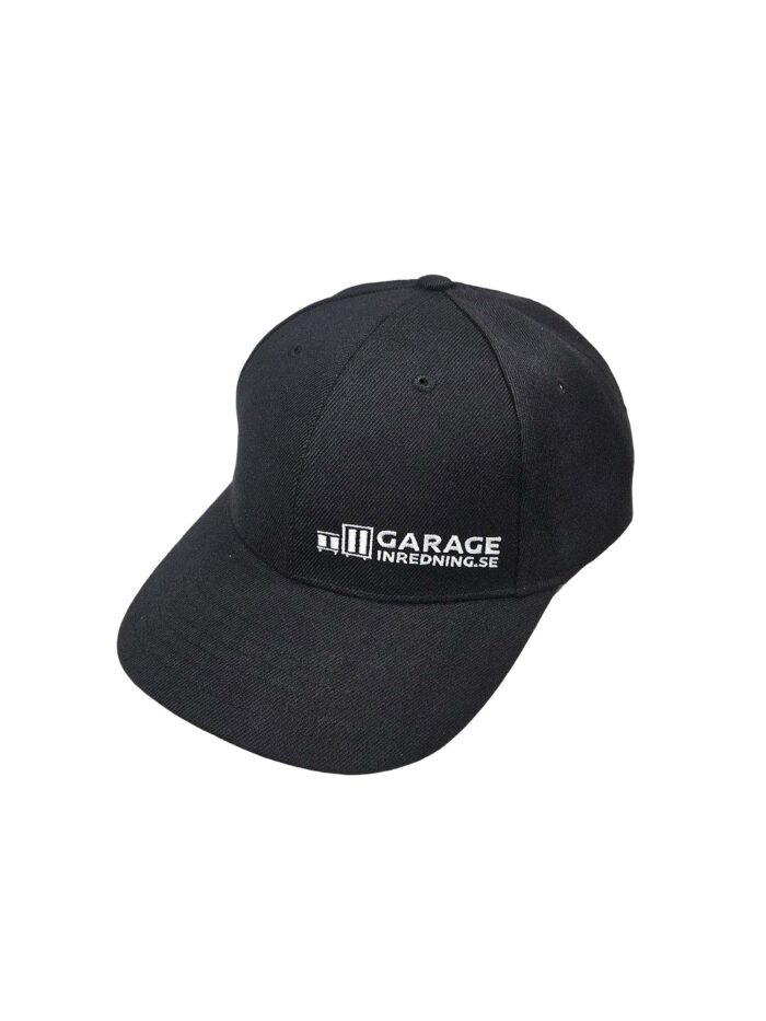 En svart snapback-keps med vit broderad text på framsidan där det står "GARAGEINREDNING.SE.