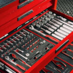 En röd verktygslåda med en öppen låda som innehåller organiserade hylsor, skiftnycklar och olika handverktyg. Verktygen är snyggt arrangerade i svarta skuminlägg, vilket ger en ordnad och tillgänglig layout.