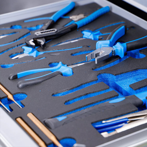 I en låda med specialskuren skumplast finns olika handverktyg med blå handtag, inklusive tänger, skiftnycklar och skruvmejslar, alla prydligt organiserade i individuella fack - perfekt för effektiv garageinredning.