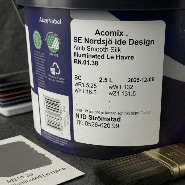 Närbild av en färgburk märkt "SE Nordsjö ide Design Amb Smooth Silk Illuminated Le Havre" med uppgifter om färgkoder, mängd och utgångsdatum. En pensel och ett färgprovskort finns i närheten.