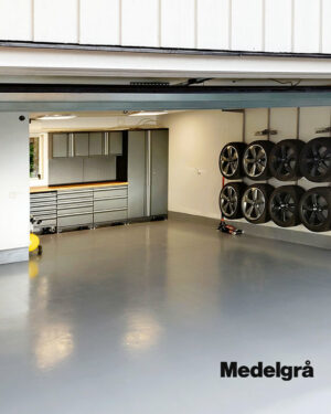 Ett rent, modernt garage med ett glänsande Epoxigolv-golv i färgen ”Medelgrå”, välorganiserade förvaringsskåp och bildäck upphängda på väggen; ”Medelgrå” syns i det nedre högra hörnet.