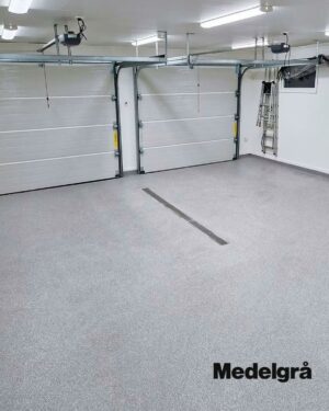 Ett rent, tomt garage med två stängda vita dörrar, ett gråspräckligt golv av Epoxigolv PRO färgsand, starka taklampor och en stege lutad mot bakväggen. I det nedre högra hörnet står det ”Medelgrå”.