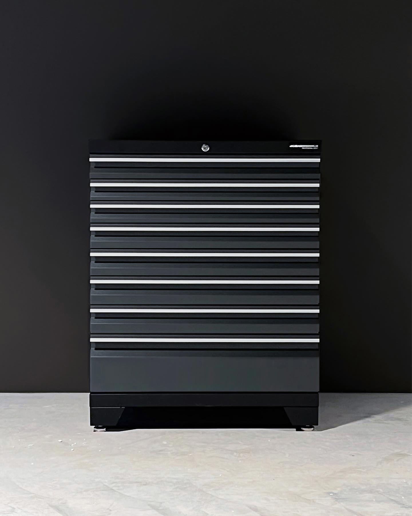En svart metallverktygslåda med åtta horisontella lådor står mot en enfärgad svart vägg på ett ljust betonggolv och är ett exempel på funktionell garageinredning för en välorganiserad arbetsplats.
